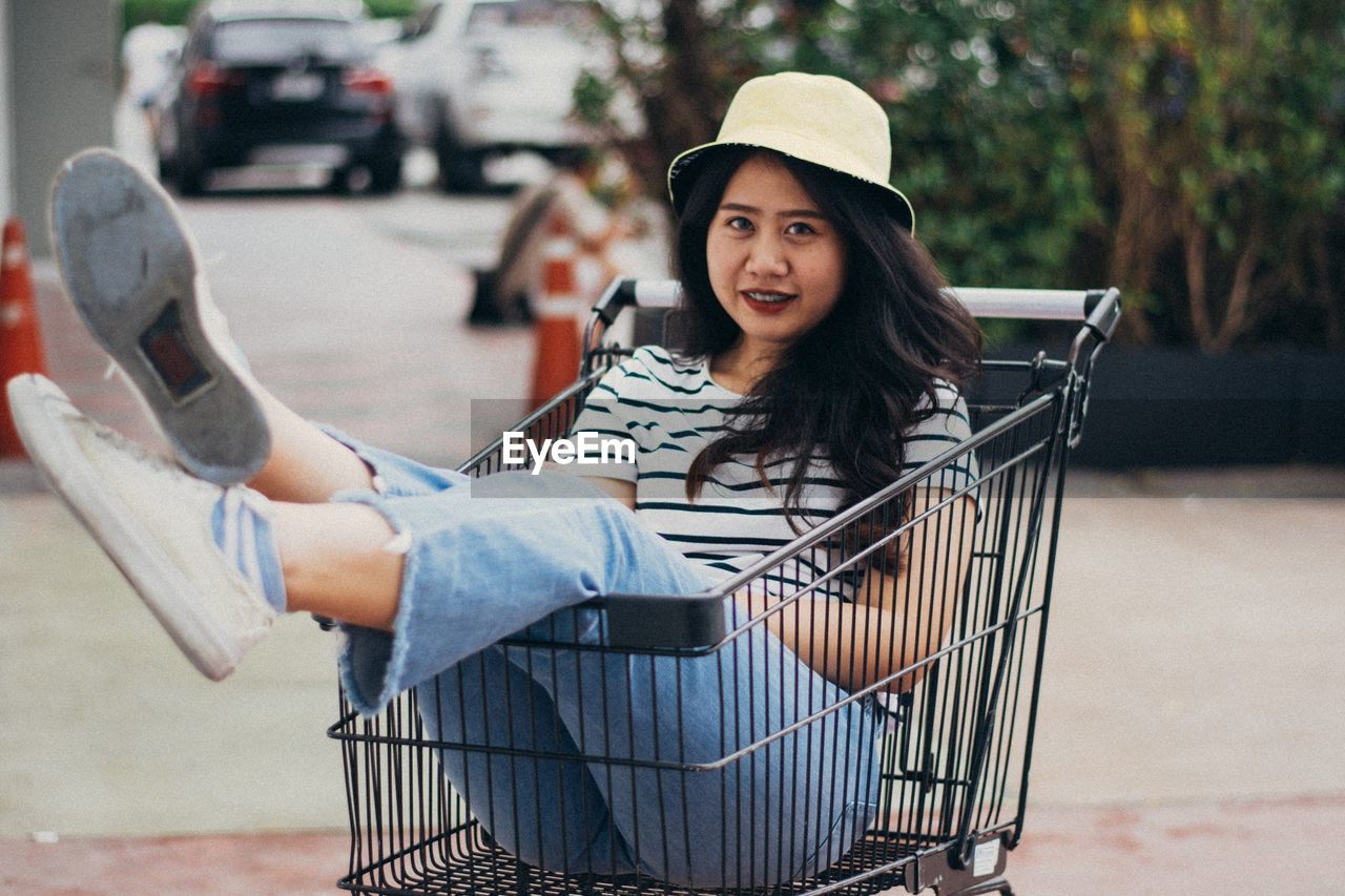 Portrait of smiling young woman sitting in shopping cart