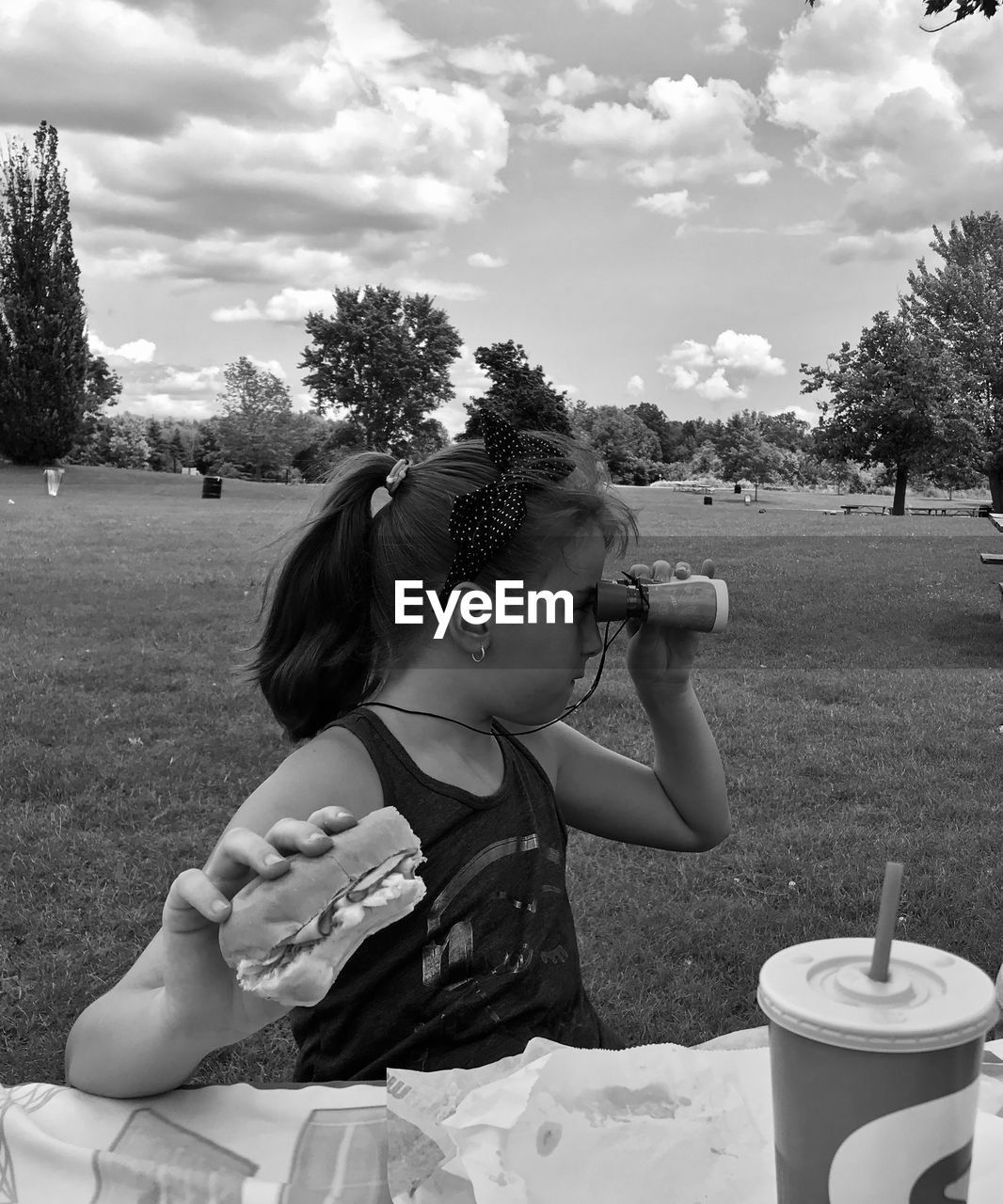 Girl holding food while looking through binoculars against sky