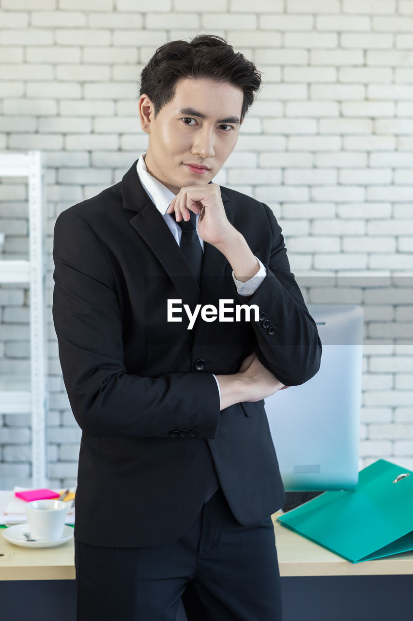 PORTRAIT OF YOUNG MAN STANDING IN FRONT OF OFFICE