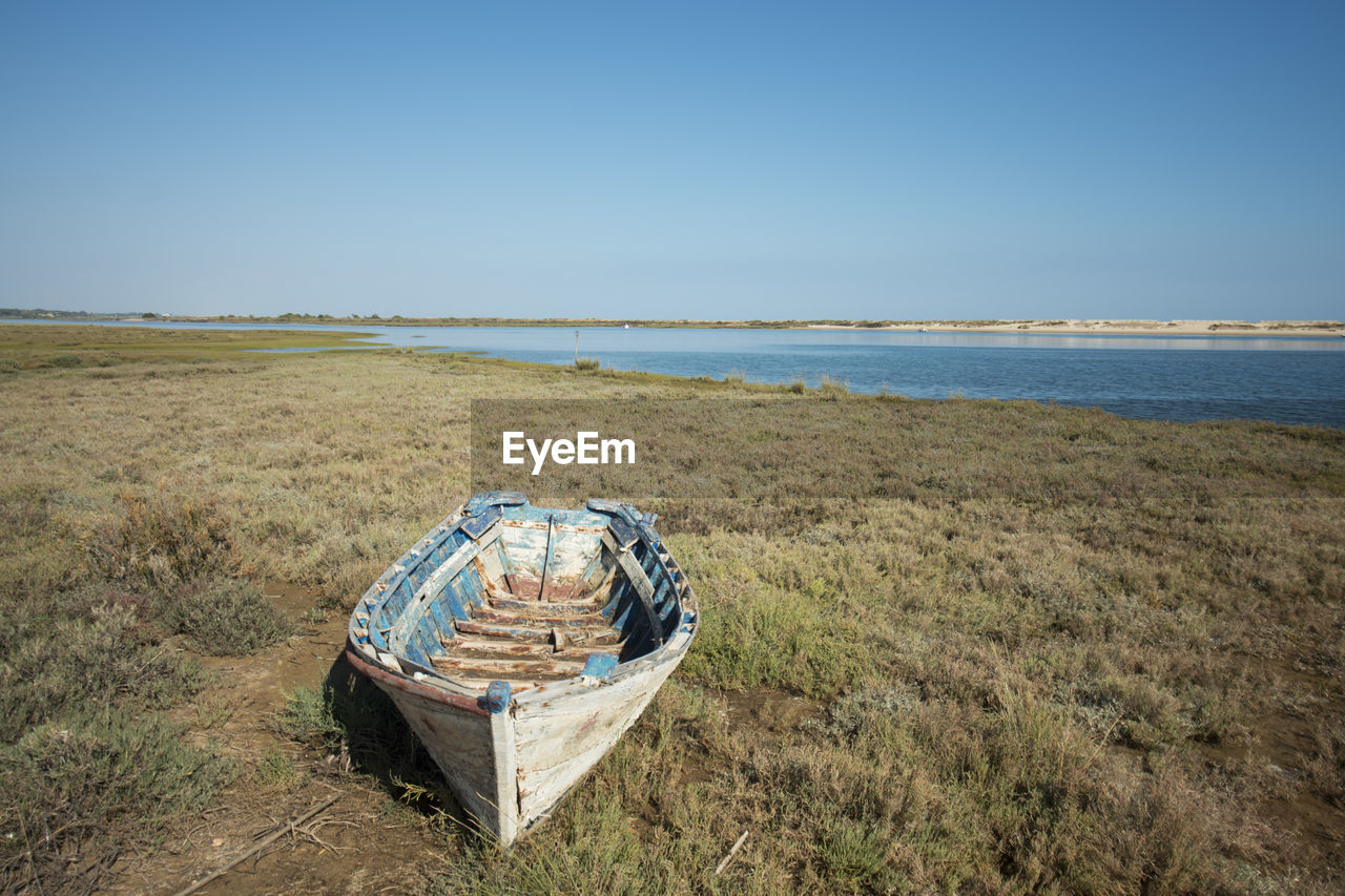 Abandoned rowboat moored on grassy seashore against clear blue sky
