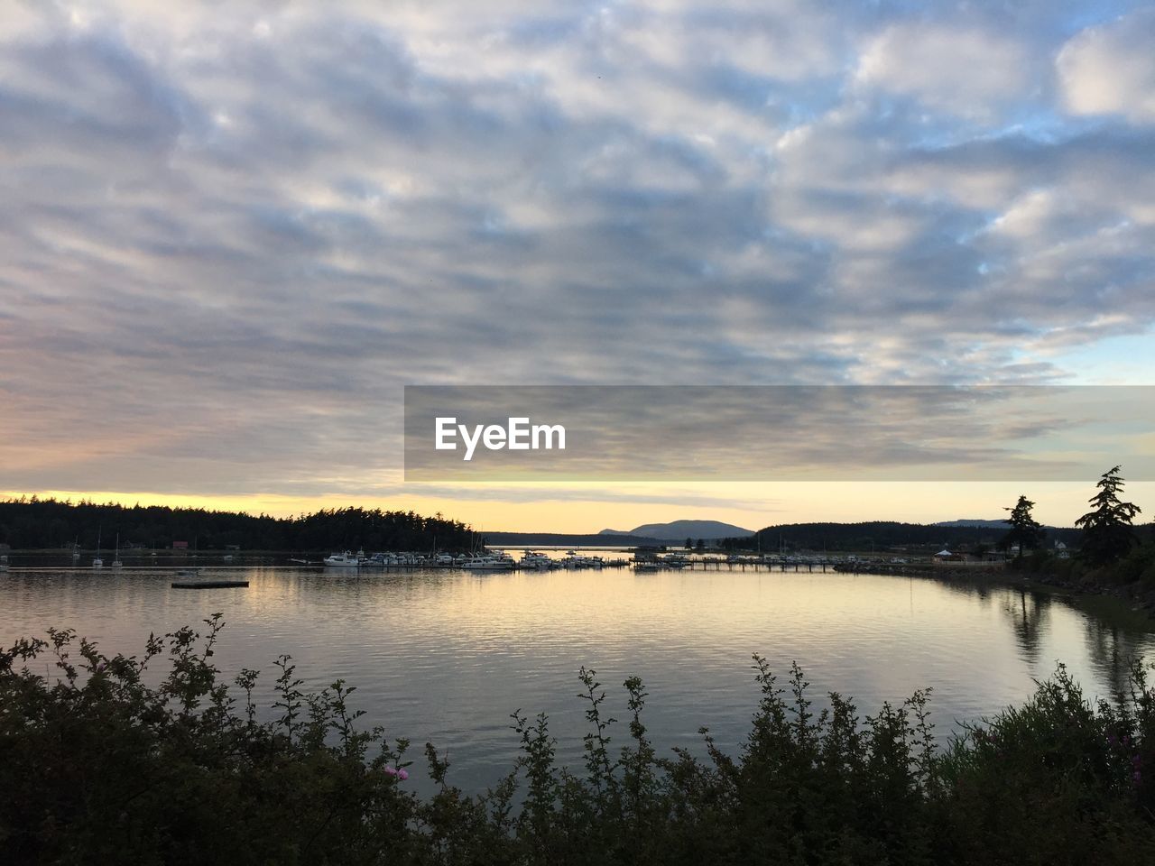 Scenic view of lake against cloudy sky during sunset