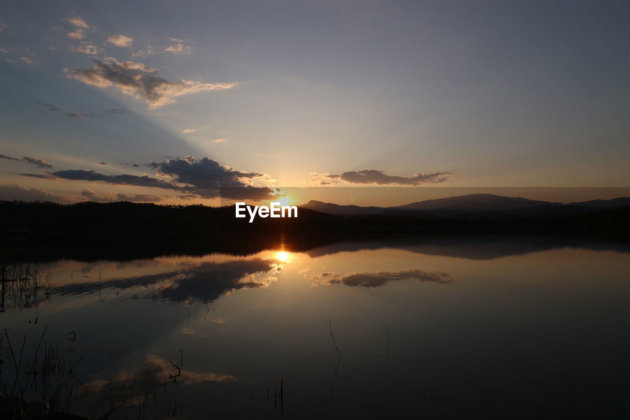 sky, water, reflection, beauty in nature, tranquility, scenics - nature, lake, tranquil scene, sunset, nature, cloud, environment, sun, no people, dawn, landscape, idyllic, mountain, sunlight, silhouette, outdoors, non-urban scene, evening, dramatic sky, afterglow, plant, orange color, land, tree, travel destinations, mountain range