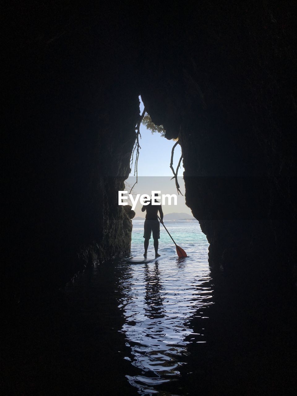 Man on paddle board in sea seen through arch