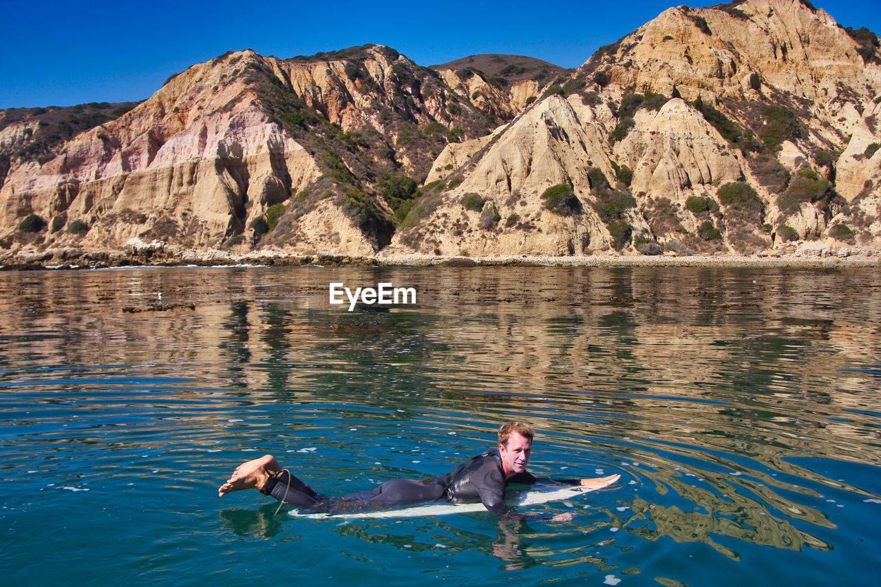 PEOPLE SWIMMING IN SEA AGAINST MOUNTAINS