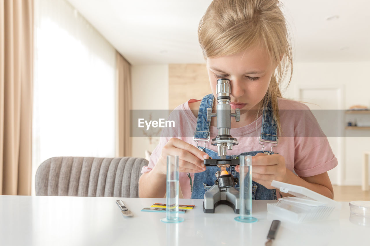 Girl looking through microscope at home