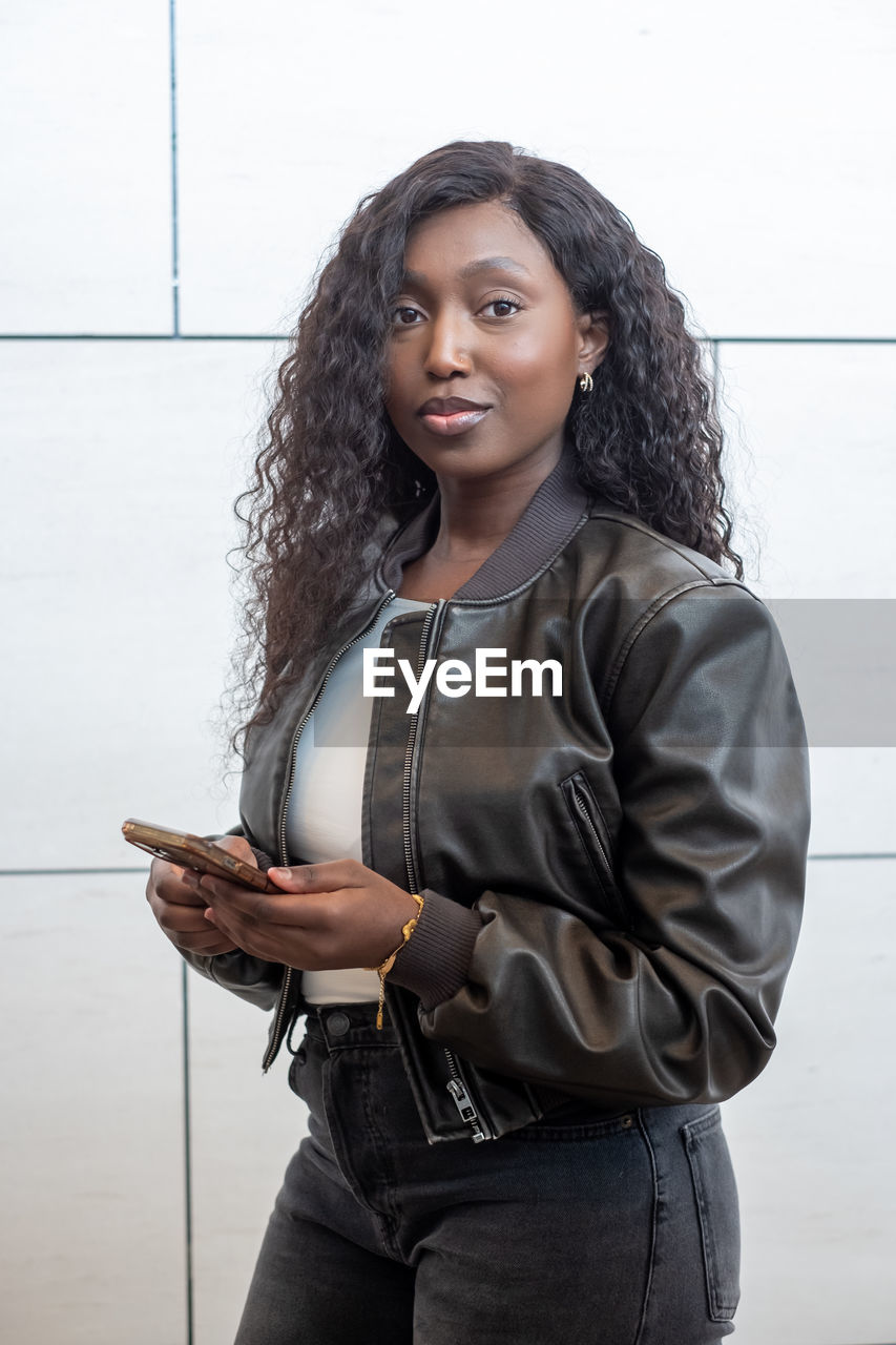 portrait of young woman using mobile phone while standing against sky