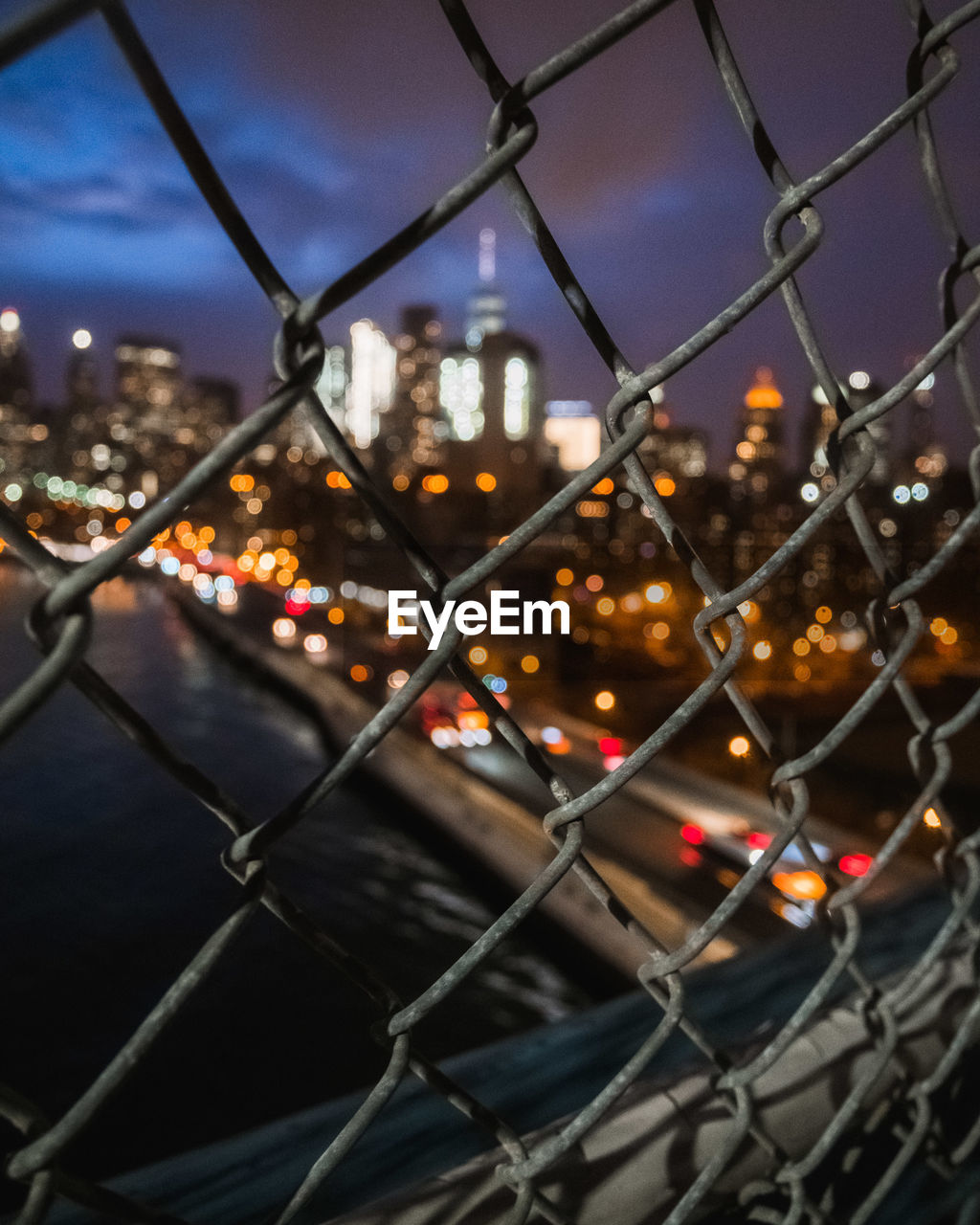 CLOSE-UP OF CHAINLINK FENCE AGAINST ILLUMINATED CITY