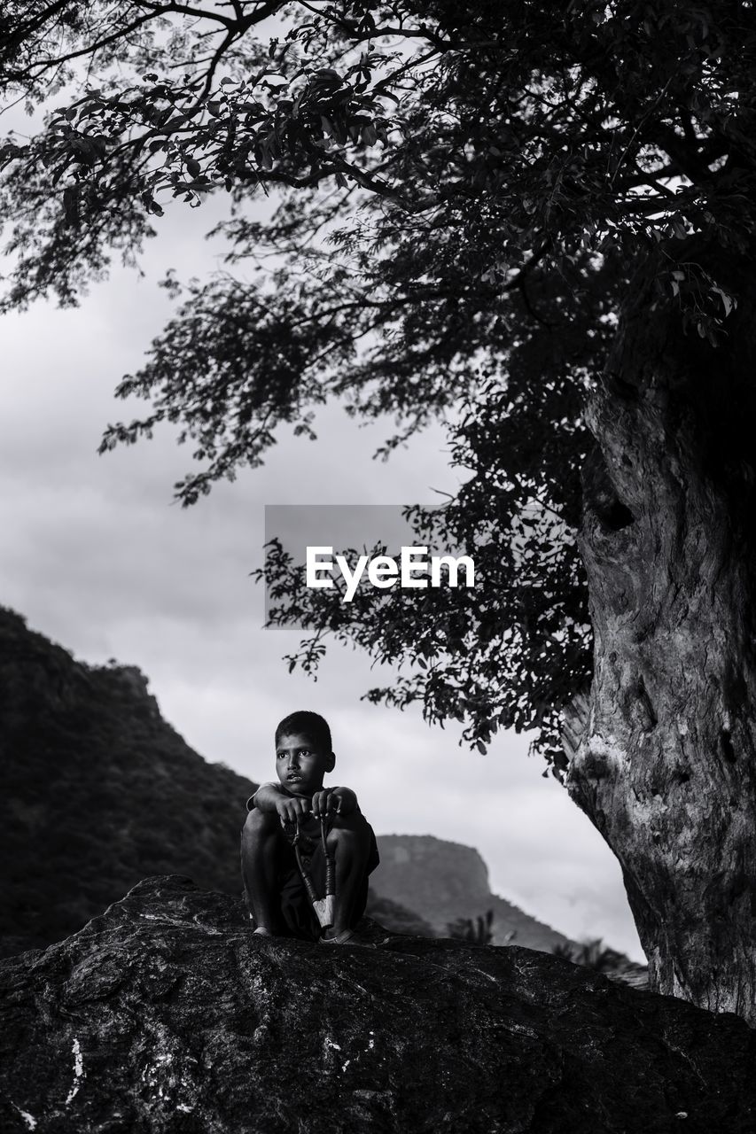 MAN SITTING ON ROCK AGAINST SKY