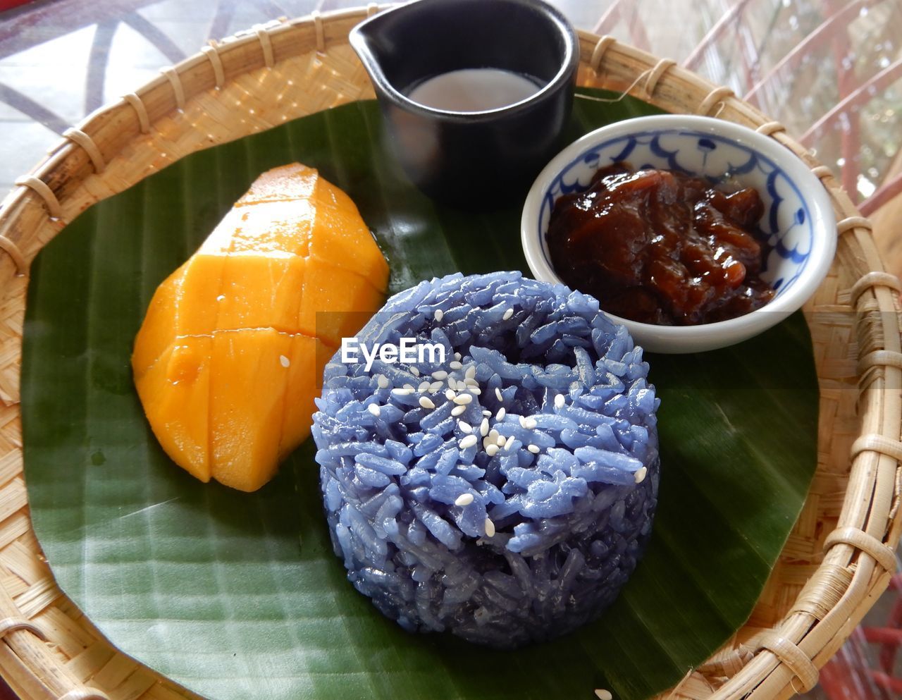 High angle view of mango fruit, blue sticky rice and marmalade with cream, served in a basket .