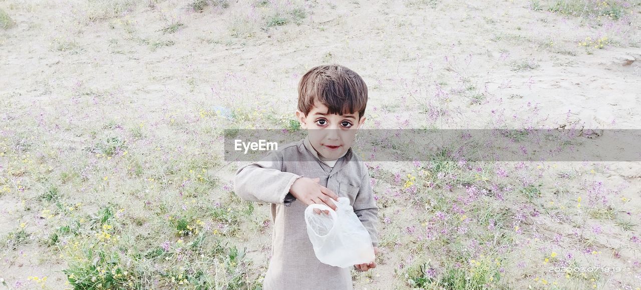 Portrait of boy holding plastic bag while standing outdoors
