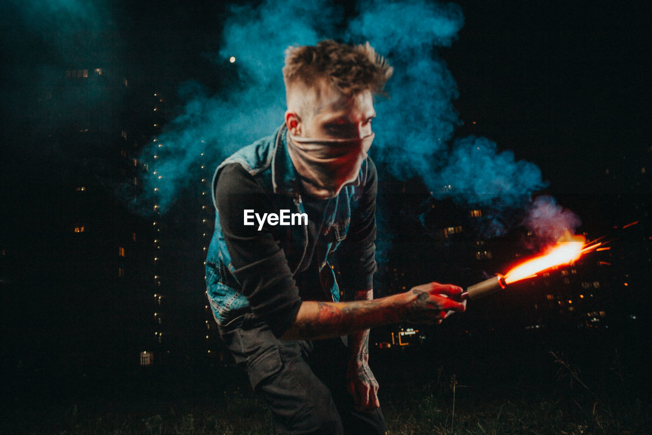 Young man wearing mask holding blow torch at night