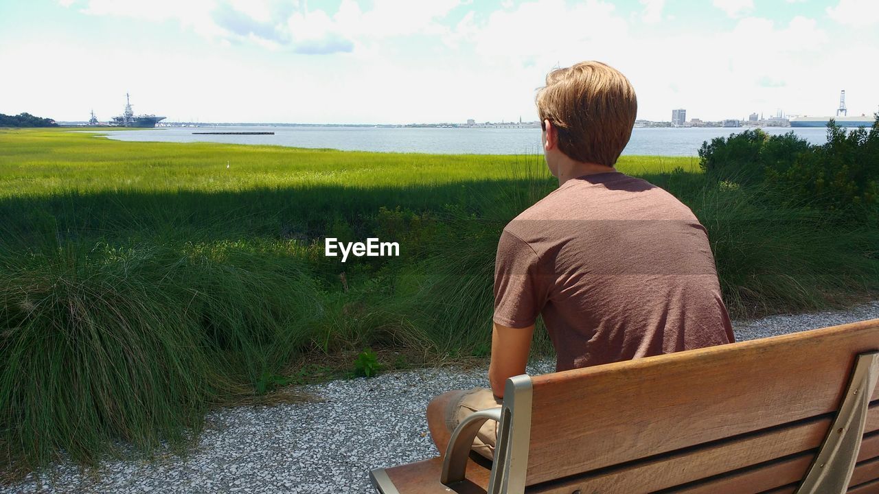 Rear view of man sitting on bench while looking at sea