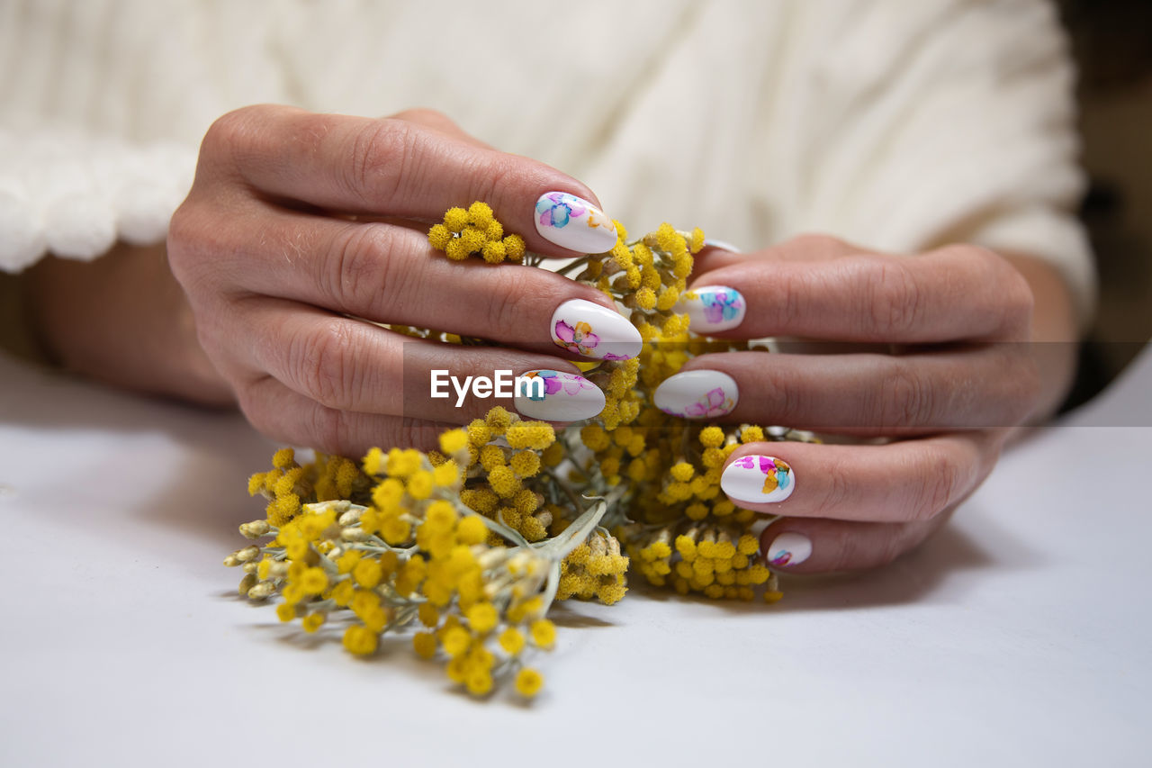 Hands with a beautiful multi-colored manicure hold a bouquet of yellow flowers