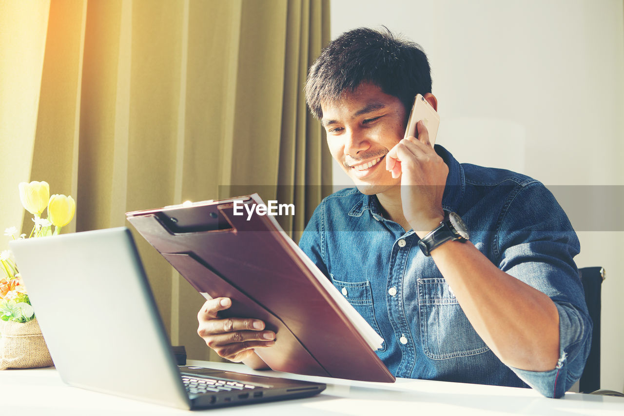 MAN USING SMART PHONE WHILE SITTING ON TABLE