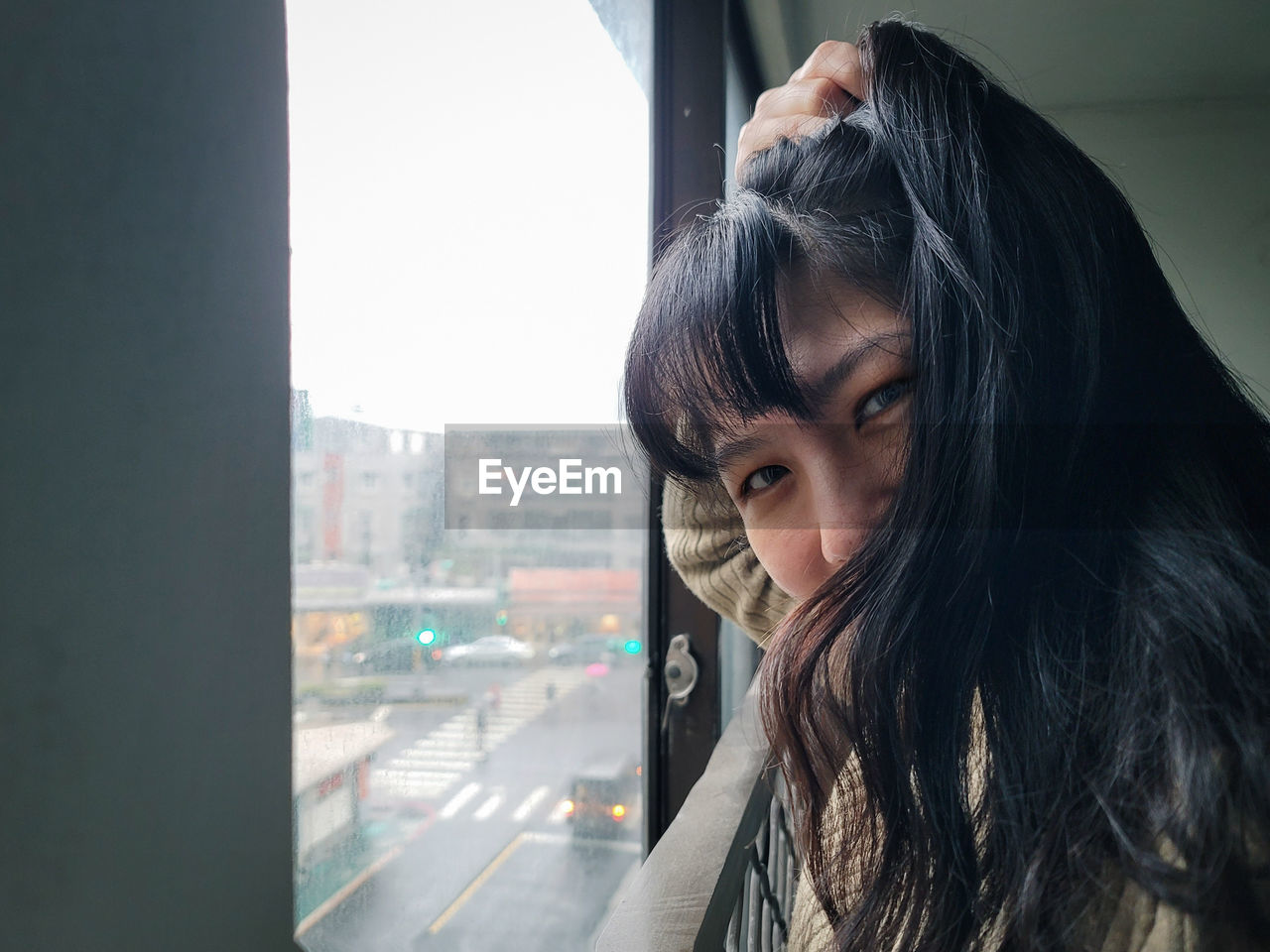 one person, portrait, adult, headshot, city, architecture, window, women, young adult, long hair, hairstyle, black hair, indoors, looking, female, built structure, day, city life, photo shoot, person, contemplation, looking through window, blue, human hair, building, lifestyles, emotion, cityscape, human face, black