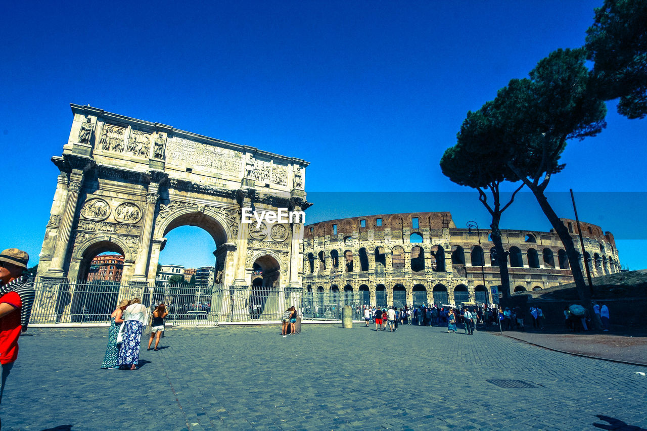 Tourists traveling at coliseum against clear blue sky