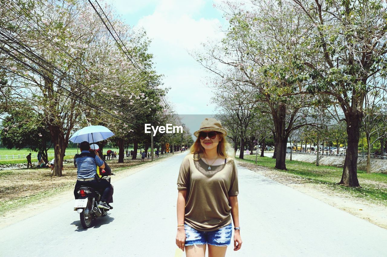 Portrait of smiling woman standing on road against trees