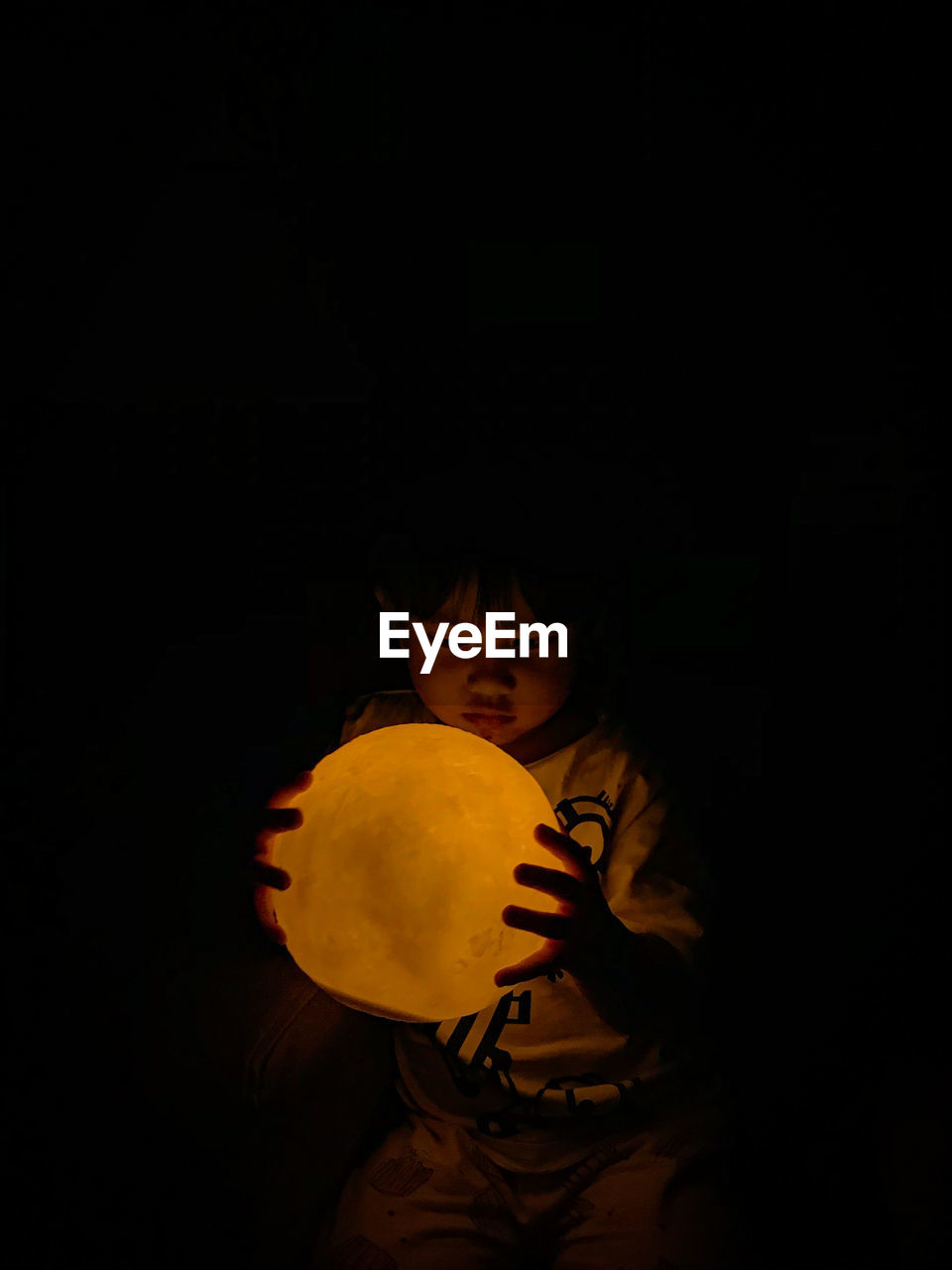 Low angle view of a child holding a moon lamp against black background