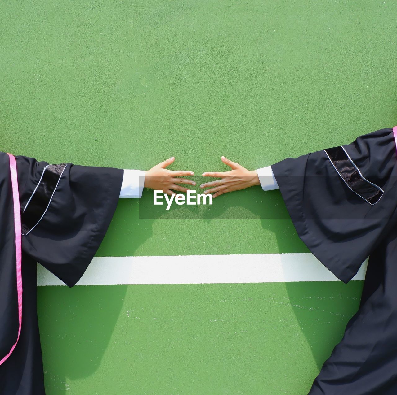 Midsection of students in graduation gowns standing against wall