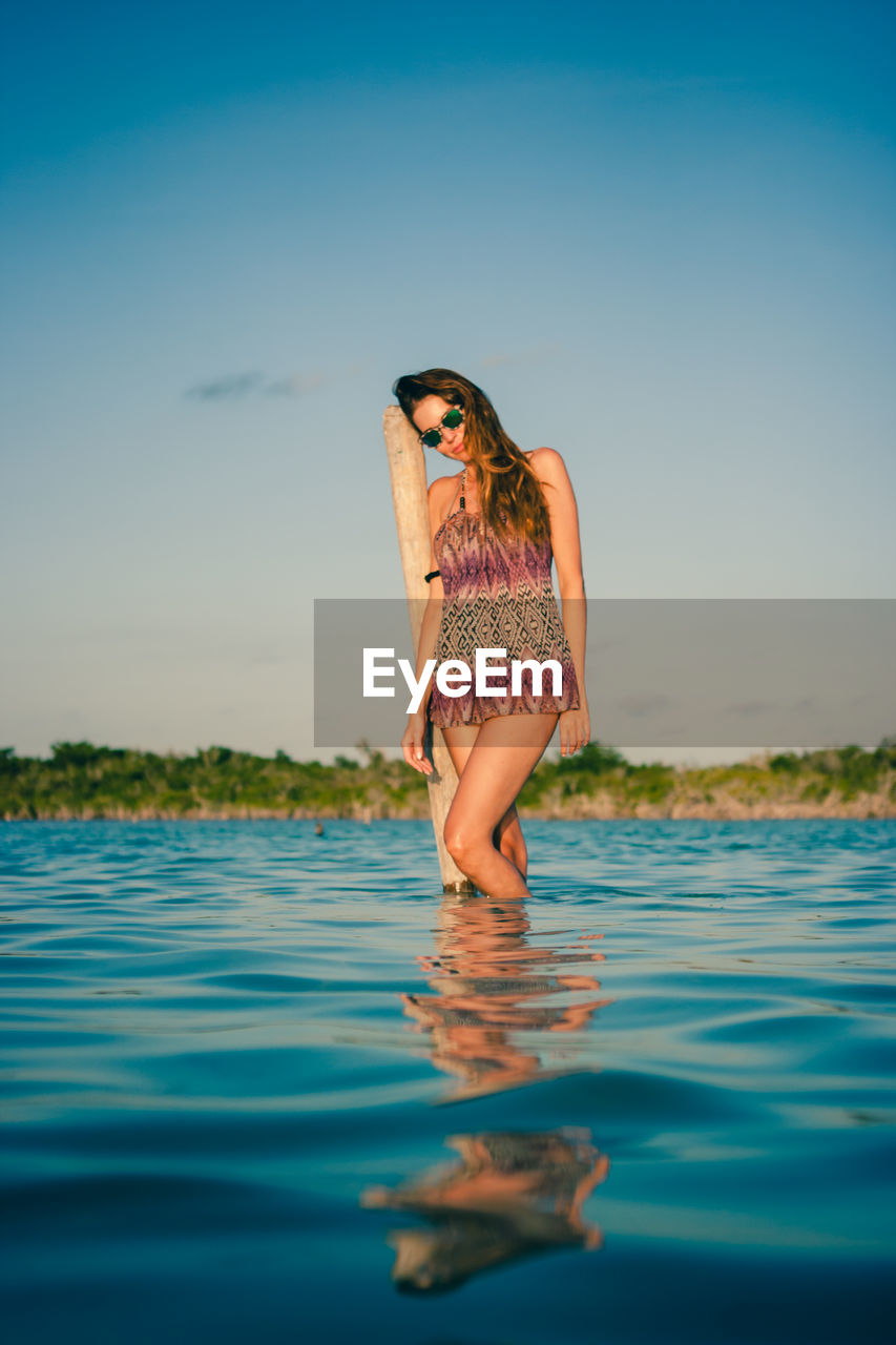 WOMAN STANDING IN SEA AGAINST CLEAR SKY