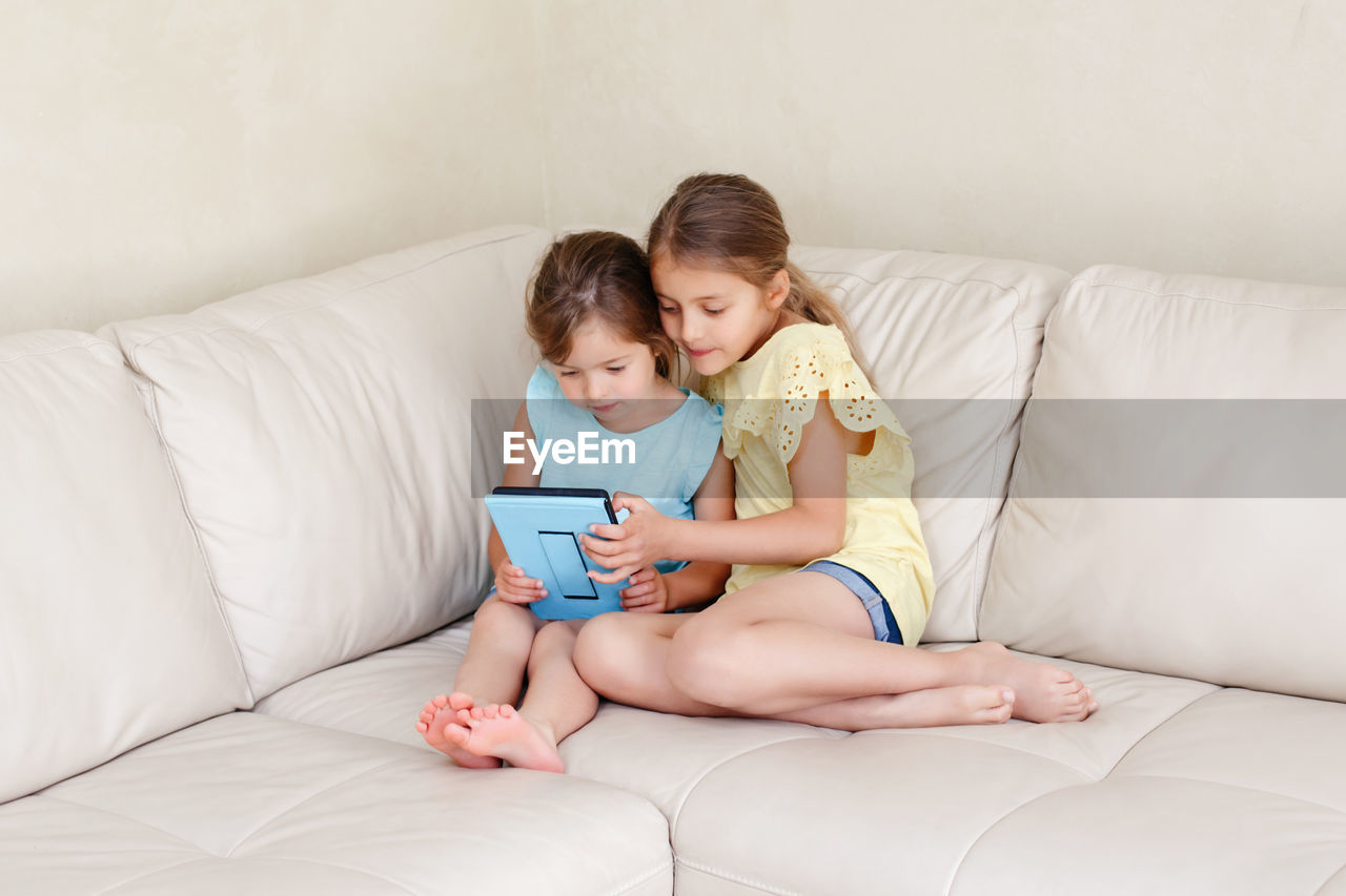 Full length of sibling using digital tablet while sitting in sofa