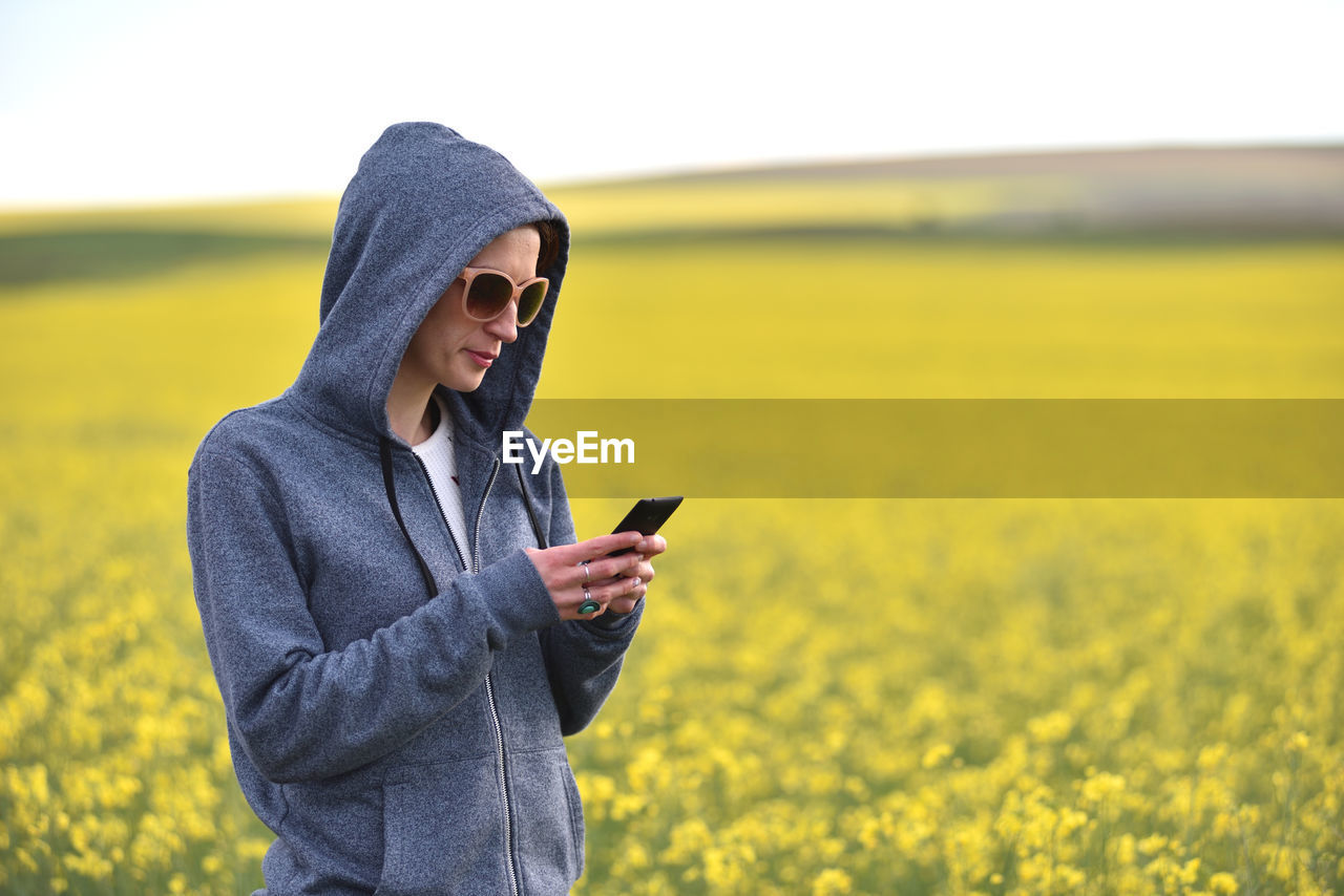 Teenager girl texting a message on her smart phone. yellow canola field in the background