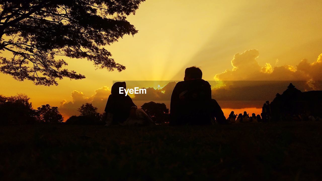 Silhouette people on field against sky during sunset