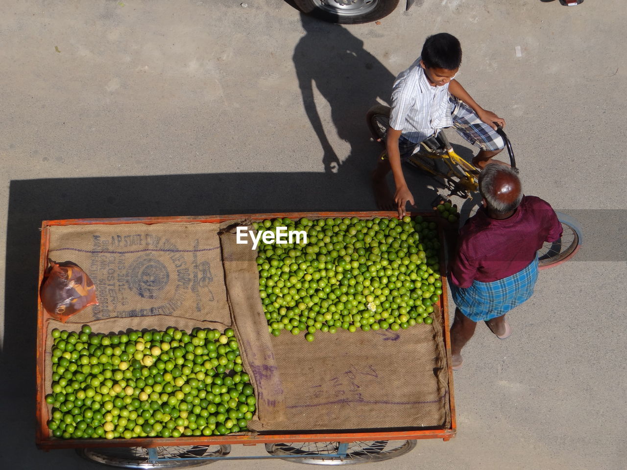 High angle view of boy buying lemons from market vendor on street in city during sunny day