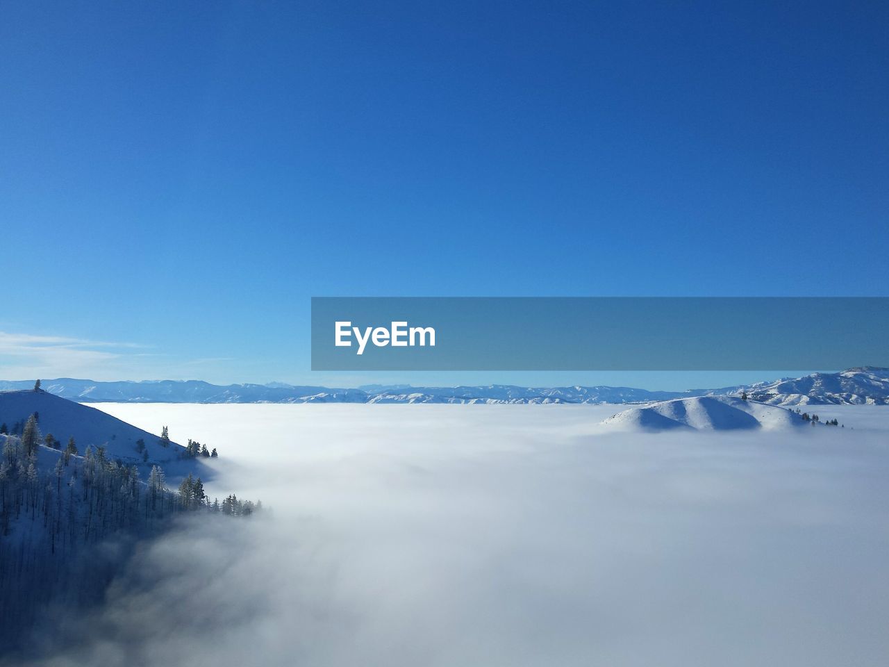 Scenic view of a sea of,clouds with snowy mountains protruding against clear blue sky