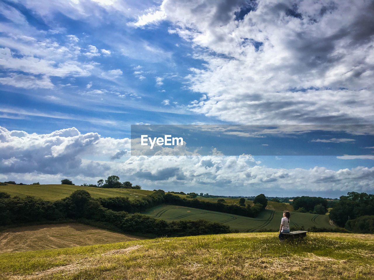 Scenic view of field against sky and a girl on a bench