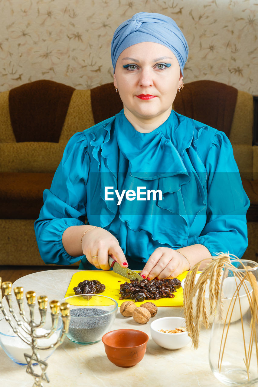 one person, adult, portrait, women, food and drink, looking at camera, indoors, food, person, front view, table, clothing, female, sitting, wellbeing, lifestyles, young adult, furniture, headscarf, human face, healthy eating, occupation, bowl, meal, waist up, cook