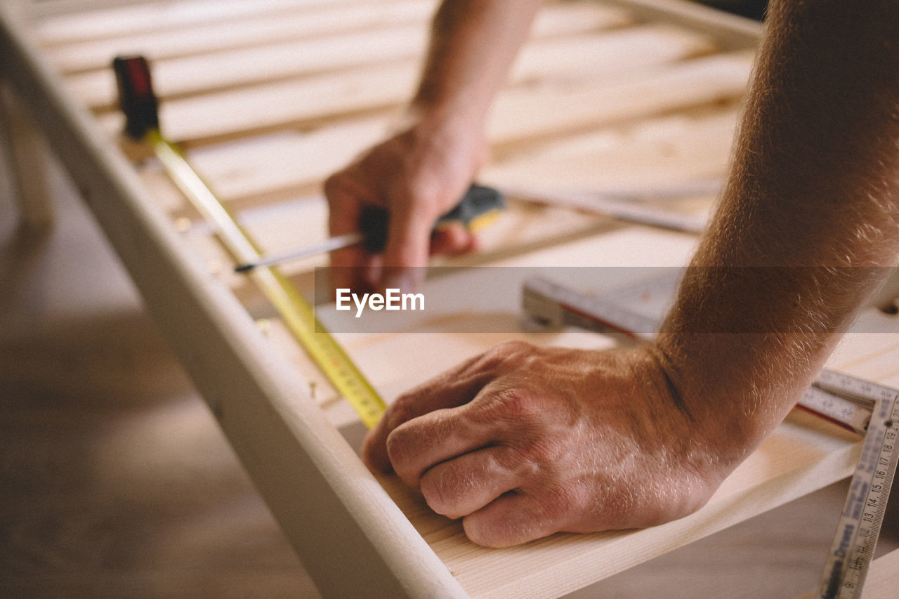 Cropped hands of man measuring wood at home