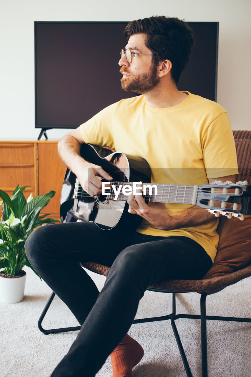 Man looking away while playing guitar at home