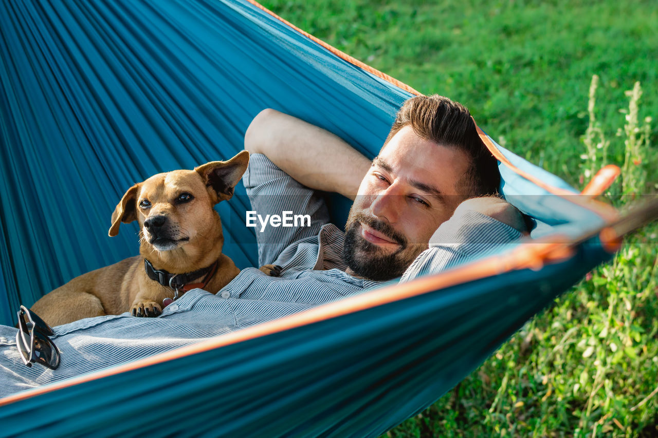 Portrait of attractive european man on hammock with cute sleepy dog.