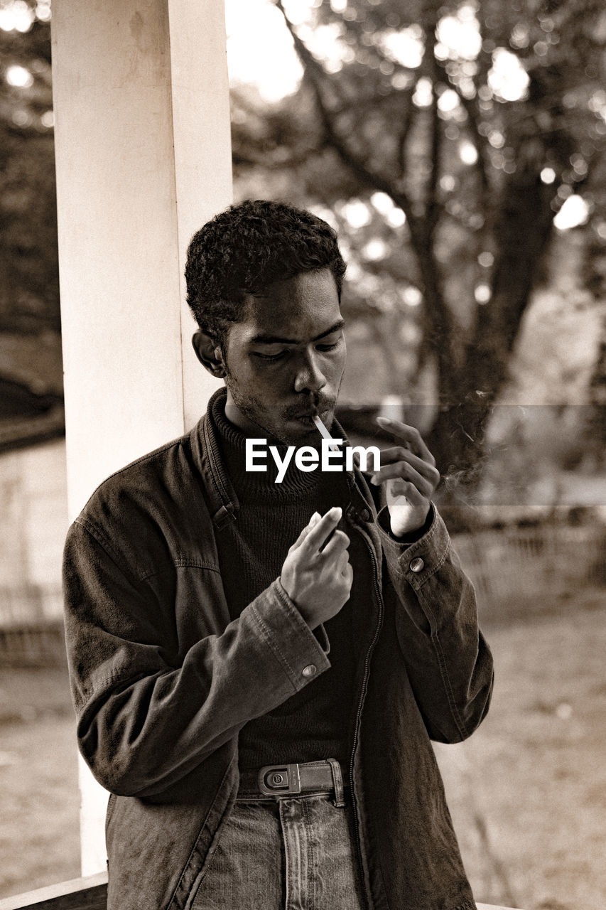 Man smoking cigarette while standing against trees