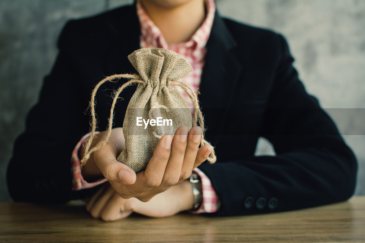 Midsection of businesswoman holding coins in sack on table