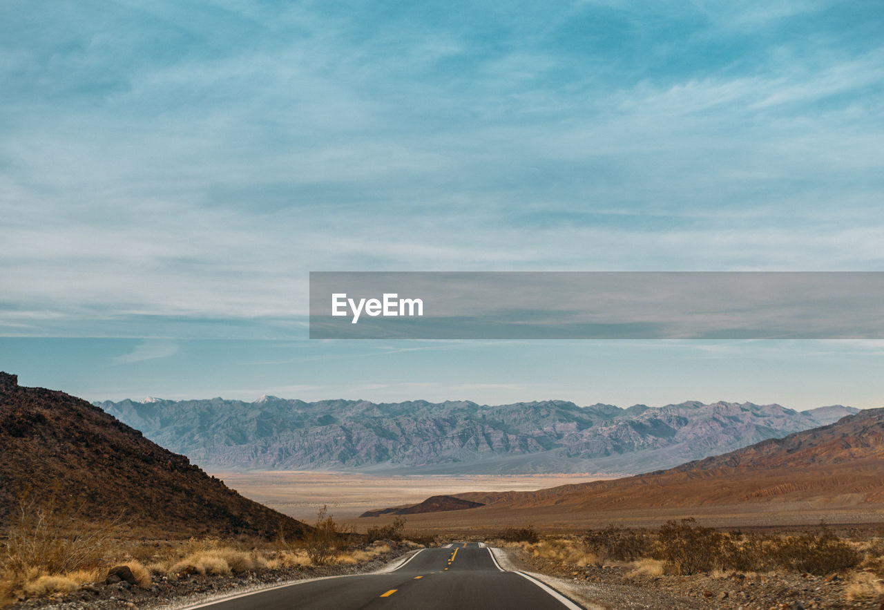 Road leading towards mountains against sky