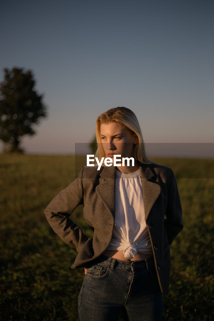 Young woman looking away while standing on field against sky