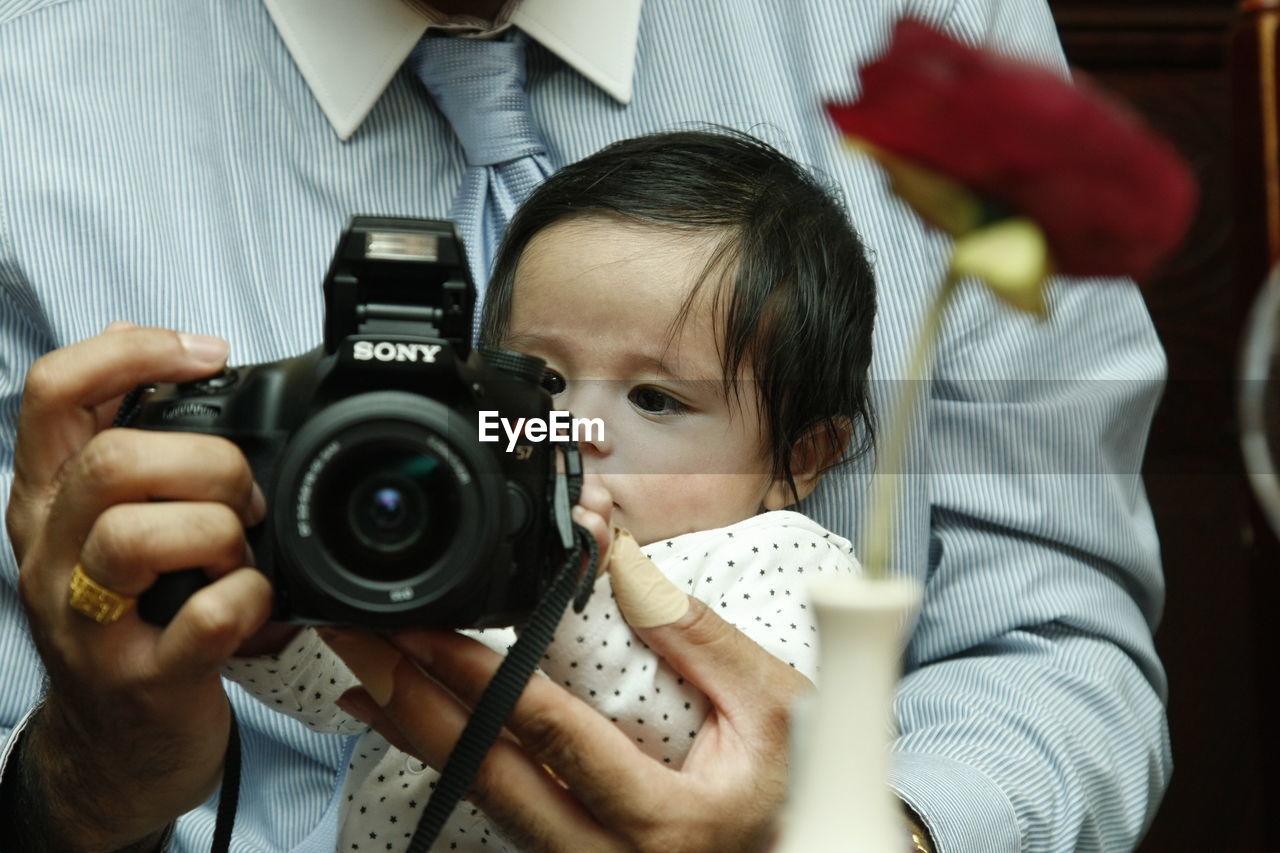 Man with camera carrying baby while sitting on sofa