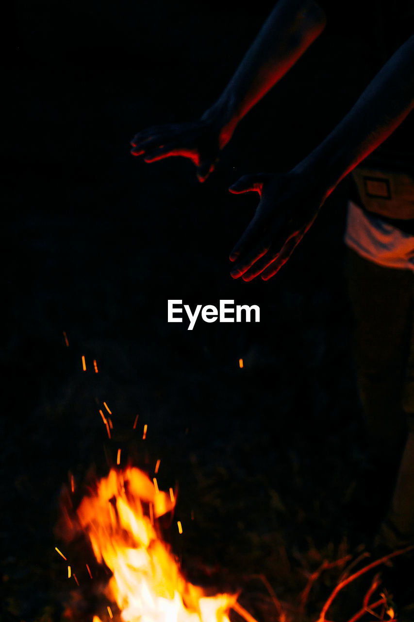 Cropped hands of person reaching bonfire at night
