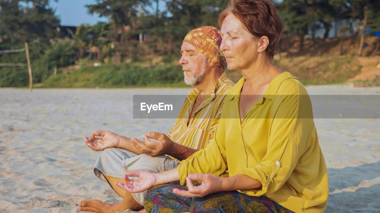 Man and woman meditating while sitting at beach