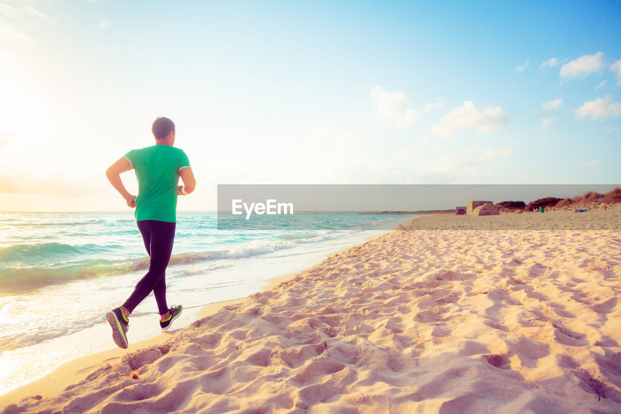 Rear view of man running at beach against sky