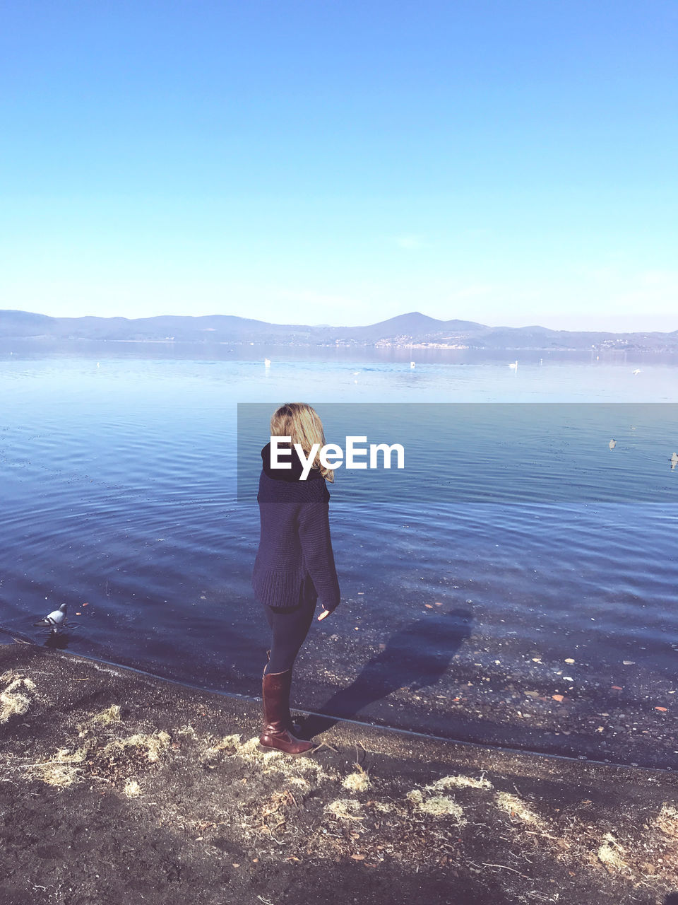 REAR VIEW OF WOMAN STANDING AT SEA SHORE AGAINST SKY