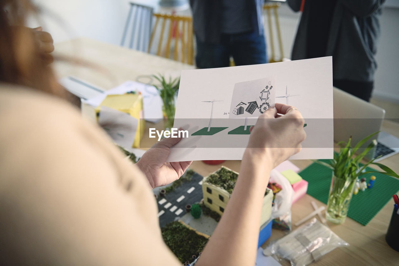 Cropped image of female engineer holding diagrams at table in office