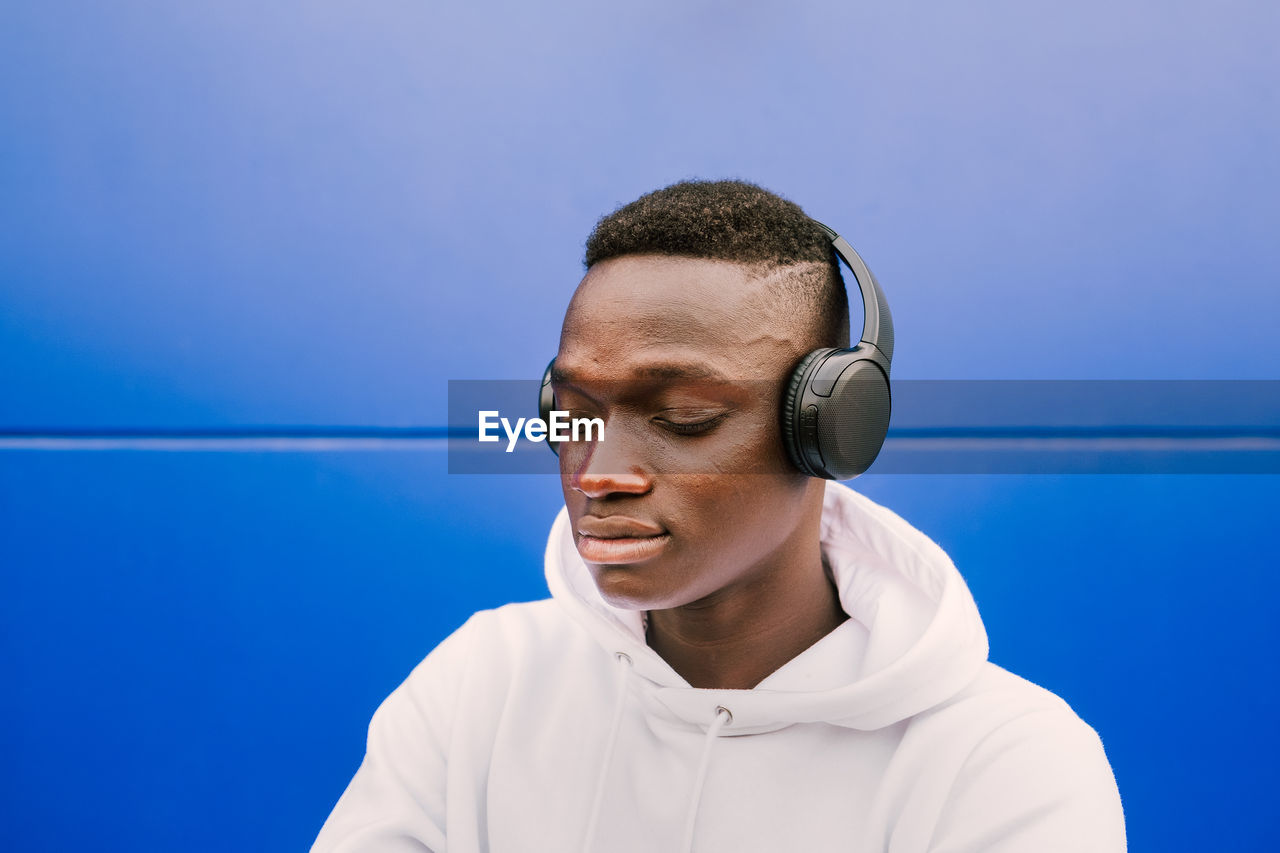 Portrait of young man wearing headphones against blue wall