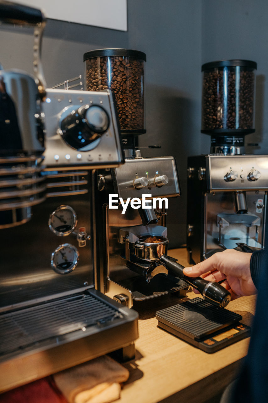 Crop unrecognizable barista using coffee grinder while preparing aromatic fresh coffee in cafe in daytime