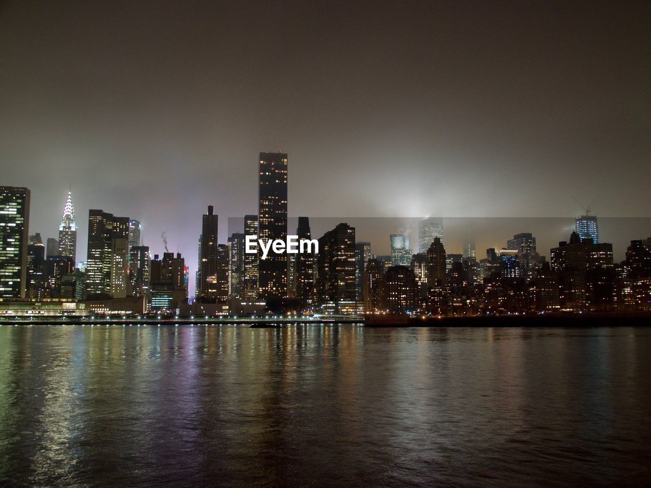 Illuminated buildings by river against sky at night