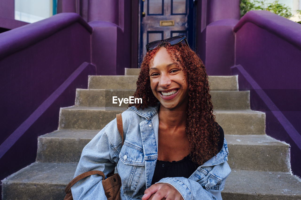 Happy young woman with curly hair sitting on staircase