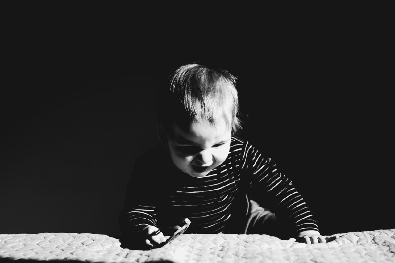Toddler boy climbing on bed in darkroom