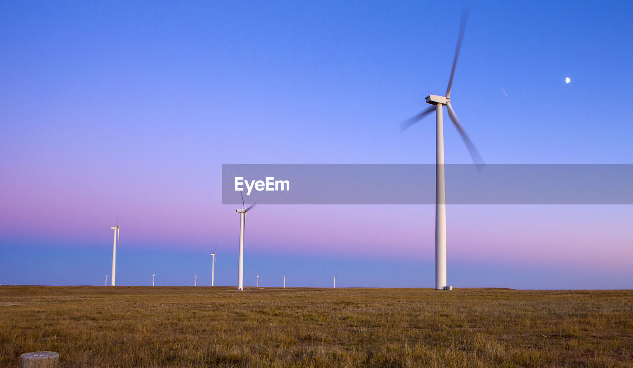 Wind turbines in field against blue sky with moon